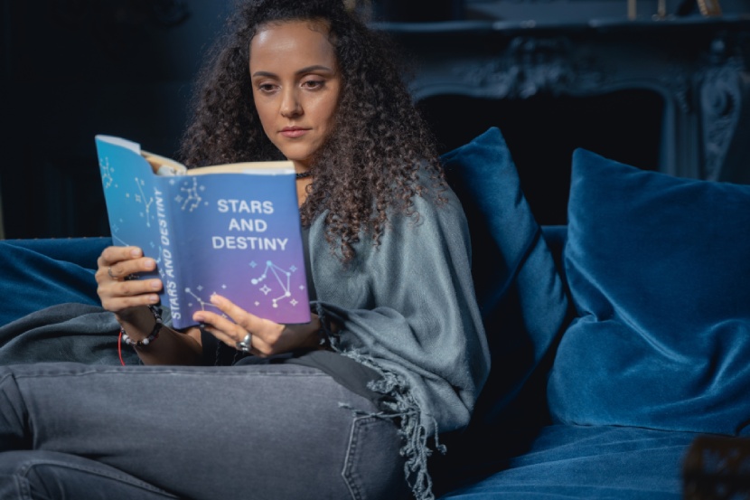 Young woman reading an astrology book on where to live based on your Zodiac sign